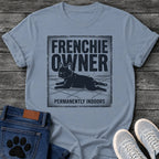 French Bulldog t-shirt with vintage distressed poster frame, bold oversized text reading Frenchie Owner above a splooting Frenchie lying flat on tile floor, bold banner text below reading Permanently Indoors, single dark ink halftone graphic with heavy crackle texture