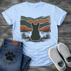 French Bulldog t-shirt with Frenchie silhouette seen from behind with cream outline sitting in grass and shallow water, bold woodcut style wavy landscape in forest green and terracotta behind, heavy distressed texture throughout, no text earthy art graphic