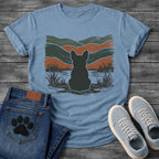 French Bulldog t-shirt with Frenchie silhouette seen from behind with cream outline sitting in grass and shallow water, bold woodcut style wavy landscape in forest green and terracotta behind, heavy distressed texture throughout, no text earthy art graphic