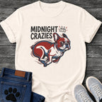 French Bulldog t-shirt with bold retro comic text reading Midnight Crazies upper left, animated alarmed clock showing 12:00 with lightning bolts and cartoon eyes, large red and blue halftone Frenchie running at full speed, speed lines throughout