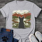 French Bulldog t-shirt with Frenchie silhouette seen from behind with cream outline, winding river flowing through a dense forest green valley, layered red and dark green mountain range behind, heavy woodcut distressed texture throughout, no text wilderness art graphic