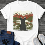 French Bulldog t-shirt with Frenchie silhouette seen from behind with cream outline, winding river flowing through a dense forest green valley, layered red and dark green mountain range behind, heavy woodcut distressed texture throughout, no text wilderness art graphic