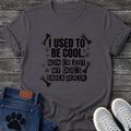 Ransom note style graphic tee design reading "I Used to Be Cool, Now I'm Just My Dog's Snack Dealer," with bones and paw prints scattered around the text.