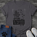 Bold stamped graphic tee design reading "The Only Therapy I Can Afford Is Talking to My Dog," with a trail of paw prints climbing the side.