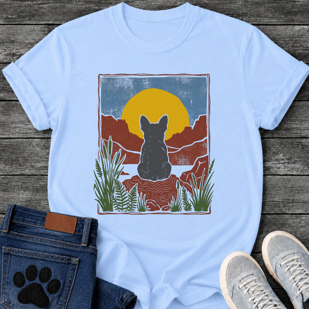 French Bulldog t-shirt with Frenchie silhouette seen from behind sitting on contoured red rock, large gold sun against slate blue sky, red canyon walls on either side, forest green ferns in foreground, distressed woodcut border frame, no text national park style art graphic