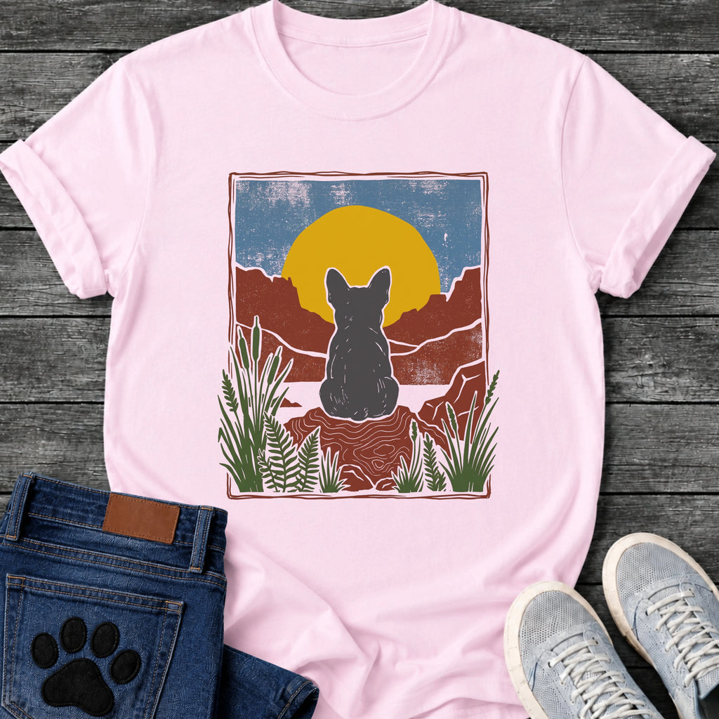 French Bulldog t-shirt with Frenchie silhouette seen from behind sitting on contoured red rock, large gold sun against slate blue sky, red canyon walls on either side, forest green ferns in foreground, distressed woodcut border frame, no text national park style art graphic