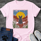French Bulldog t-shirt with Frenchie silhouette seen from behind sitting on contoured red rock, large gold sun against slate blue sky, red canyon walls on either side, forest green ferns in foreground, distressed woodcut border frame, no text national park style art graphic