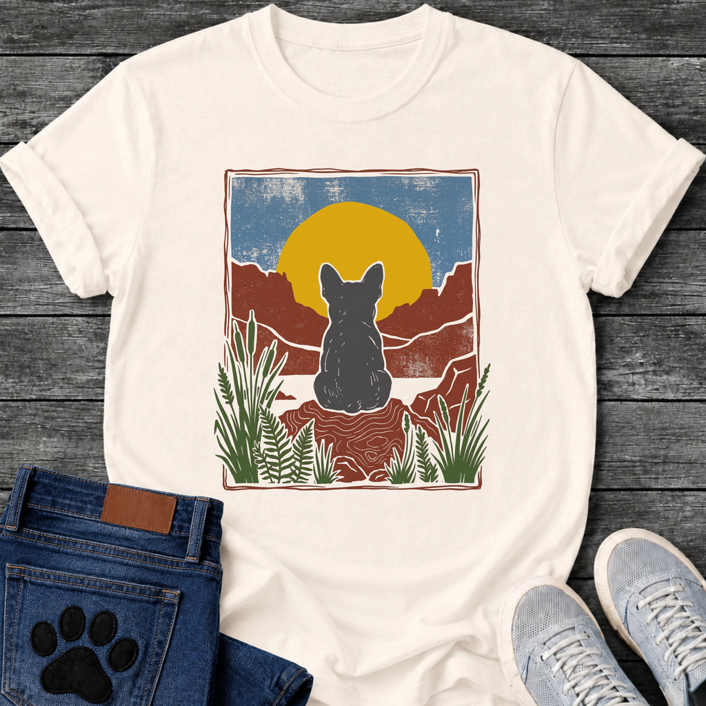 French Bulldog t-shirt with Frenchie silhouette seen from behind sitting on contoured red rock, large gold sun against slate blue sky, red canyon walls on either side, forest green ferns in foreground, distressed woodcut border frame, no text national park style art graphic