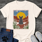 French Bulldog t-shirt with Frenchie silhouette seen from behind sitting on contoured red rock, large gold sun against slate blue sky, red canyon walls on either side, forest green ferns in foreground, distressed woodcut border frame, no text national park style art graphic
