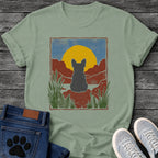 French Bulldog t-shirt with Frenchie silhouette seen from behind sitting on contoured red rock, large gold sun against slate blue sky, red canyon walls on either side, forest green ferns in foreground, distressed woodcut border frame, no text national park style art graphic