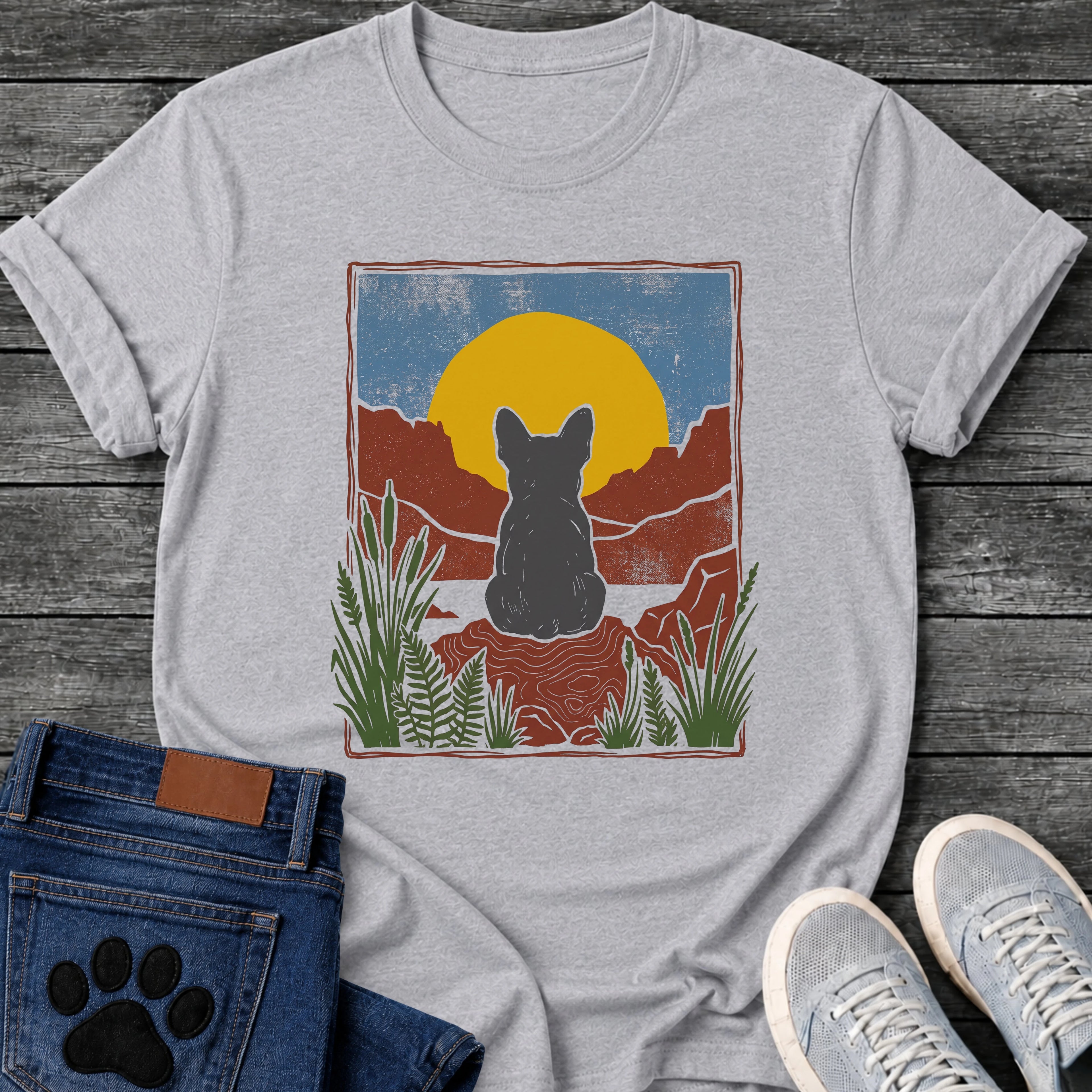 Sport GreyFrench Bulldog t-shirt with Frenchie silhouette seen from behind sitting on contoured red rock, large gold sun against slate blue sky, red canyon walls on either side, forest green ferns in foreground, distressed woodcut border frame, no text national park style art graphic