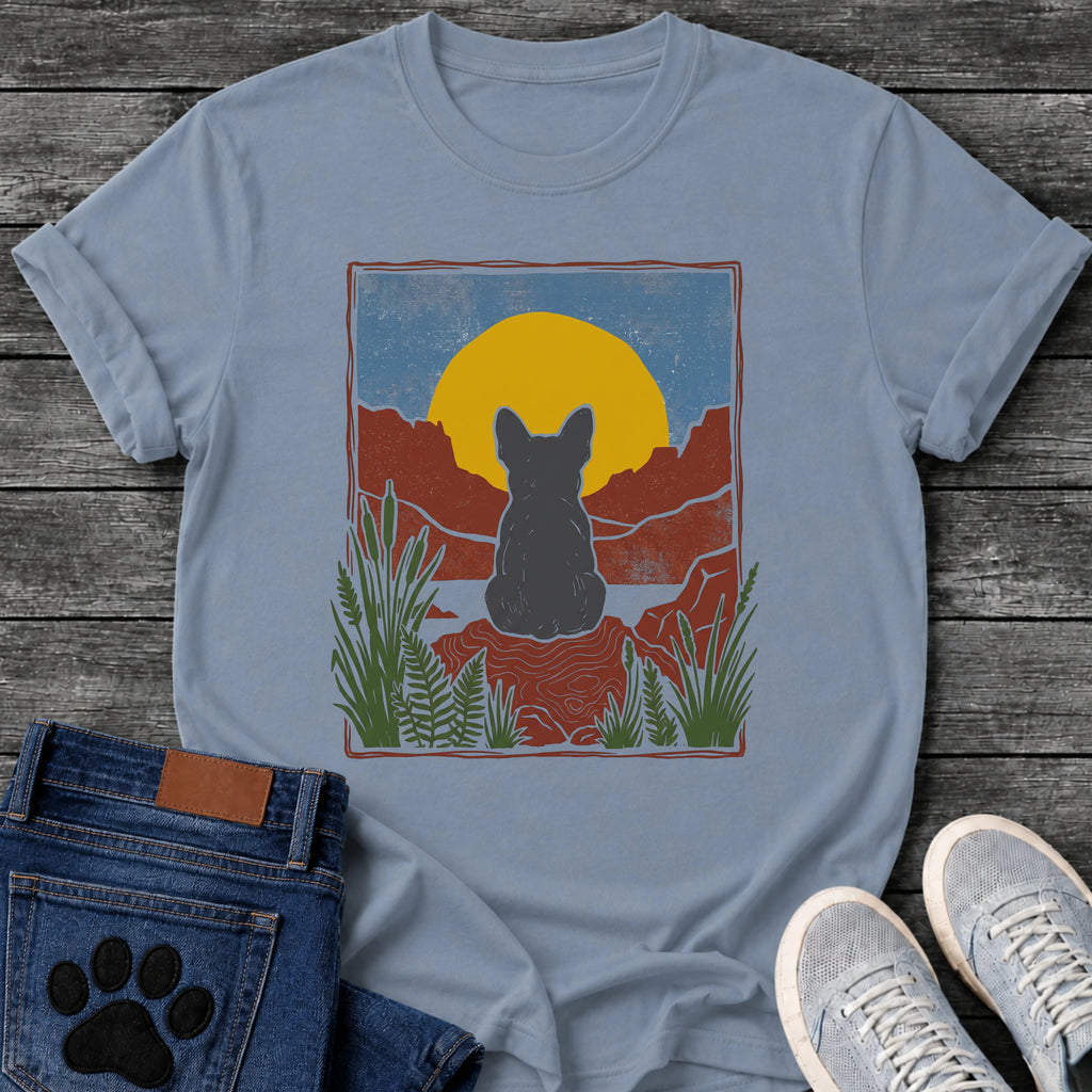 French Bulldog t-shirt with Frenchie silhouette seen from behind sitting on contoured red rock, large gold sun against slate blue sky, red canyon walls on either side, forest green ferns in foreground, distressed woodcut border frame, no text national park style art graphic