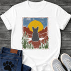 French Bulldog t-shirt with Frenchie silhouette seen from behind sitting on contoured red rock, large gold sun against slate blue sky, red canyon walls on either side, forest green ferns in foreground, distressed woodcut border frame, no text national park style art graphic