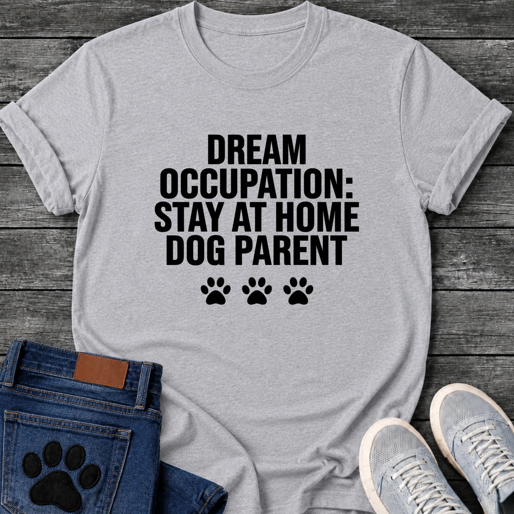 Bold block letter graphic tee design reading "Dream Occupation: Stay at Home Dog Parent," with three solid paw prints below the text.