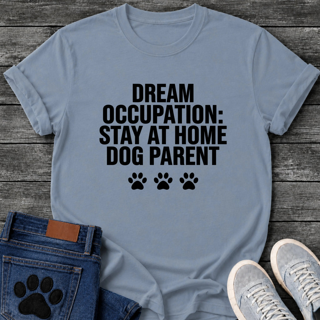 Bold block letter graphic tee design reading "Dream Occupation: Stay at Home Dog Parent," with three solid paw prints below the text.