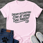 Hand script graphic tee design reading "Dream Occupation: Stay at Home Dog Parent," with a flourished underline and paw print.