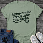 Hand script graphic tee design reading "Dream Occupation: Stay at Home Dog Parent," with a flourished underline and paw print.