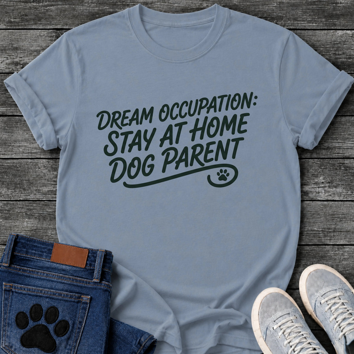 Hand script graphic tee design reading "Dream Occupation: Stay at Home Dog Parent," with a flourished underline and paw print.