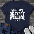 Varsity style graphic tee design in white lettering reading "World's Okayest Dog Parent," with a banner ribbon and three stars underneath.